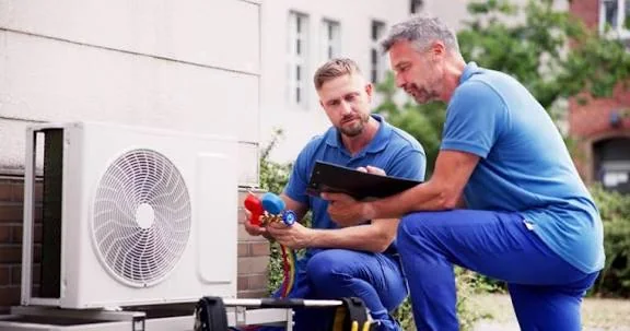 Two HVAC technicians inspecting residential outdoor cooling equipment