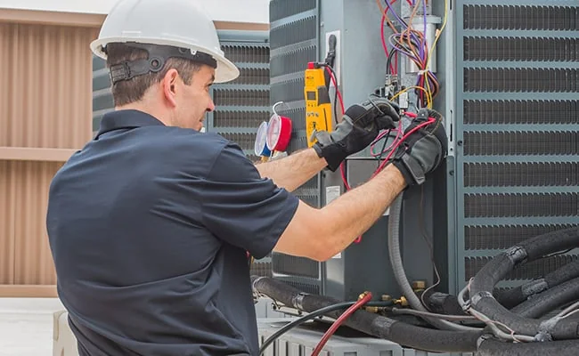 Technician diagnosing electrical connections on outdoor HVAC equipment