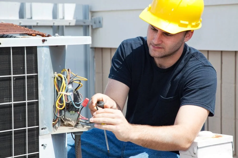 Technician repairing wiring inside an outdoor HVAC unit